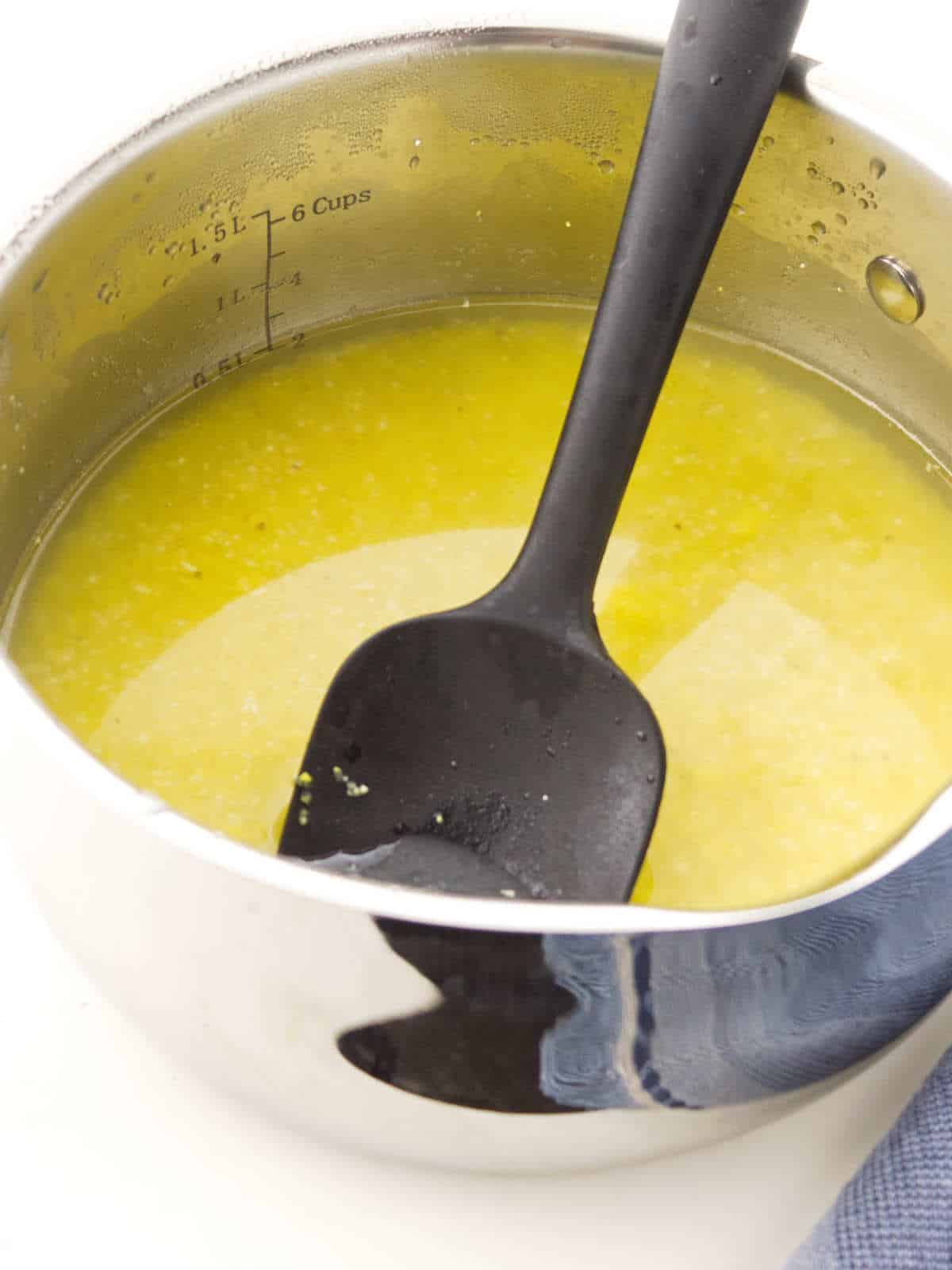 Stainless steel pot with spatula stirring cornmeal.