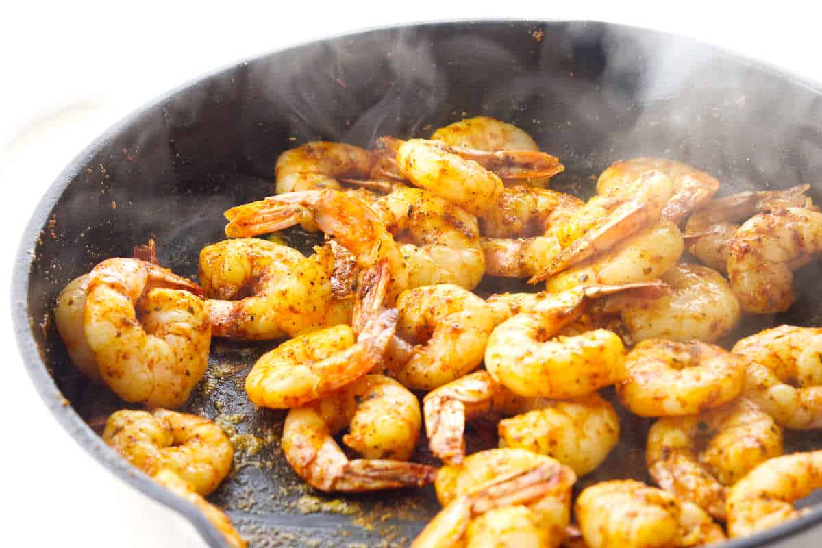 Cooked seasoned shrimp in a hot skillet with steam rising.