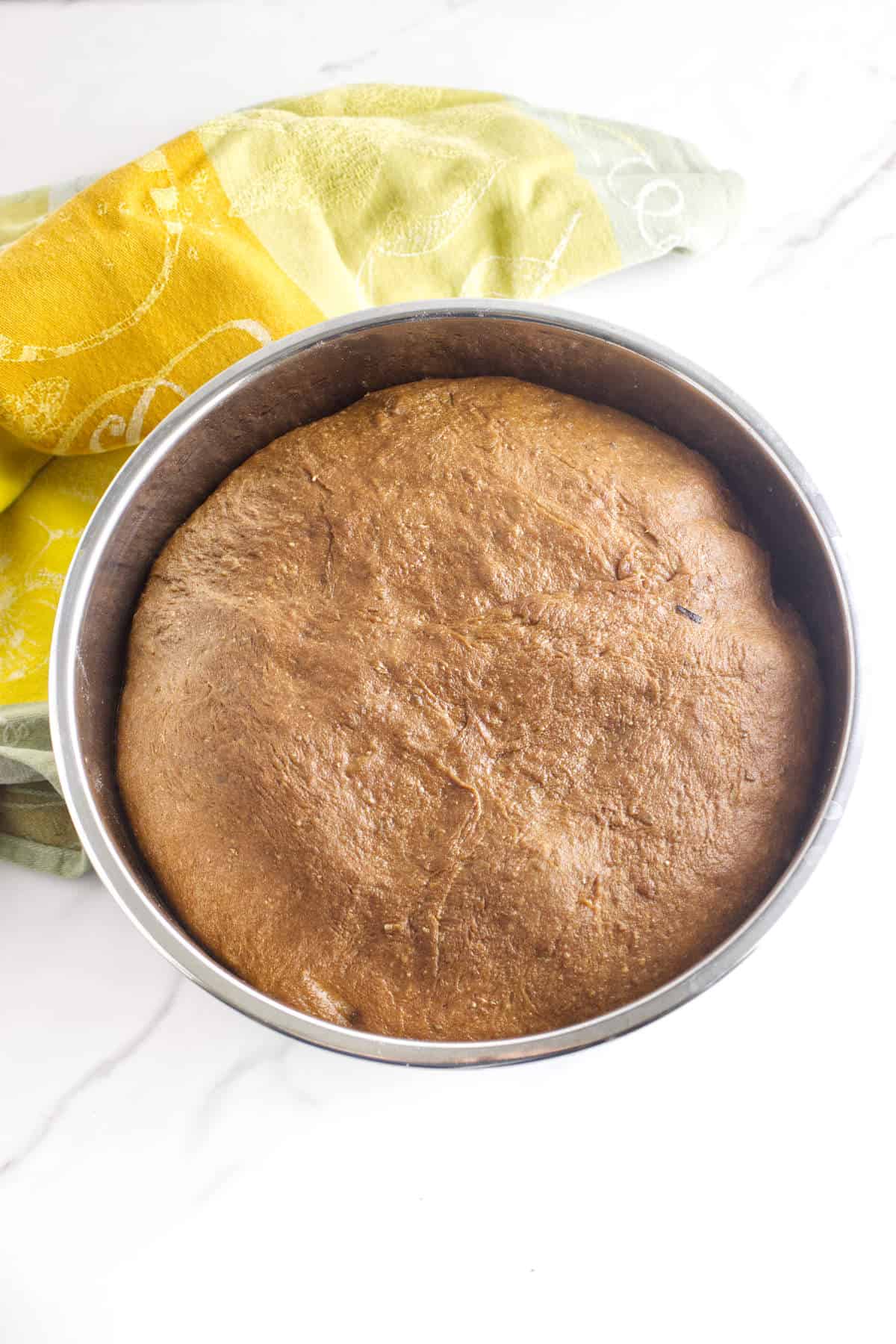 Brown bread dough rising in a metal bowl.