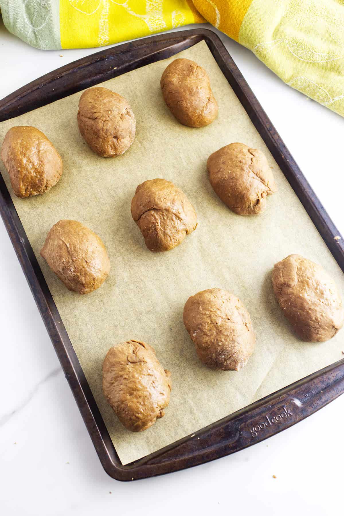 Shaped brown bread rolls on a parchment lined baking sheet.