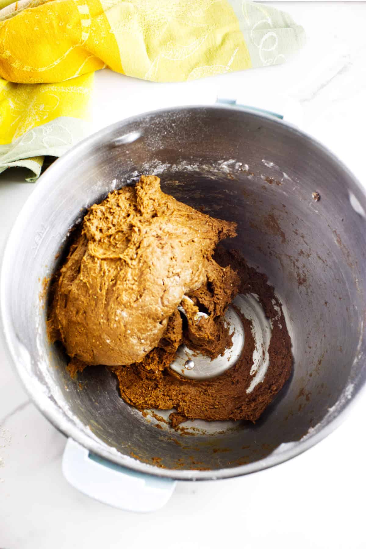 Sticky brown bread dough mixing in a stand mixer bowl.