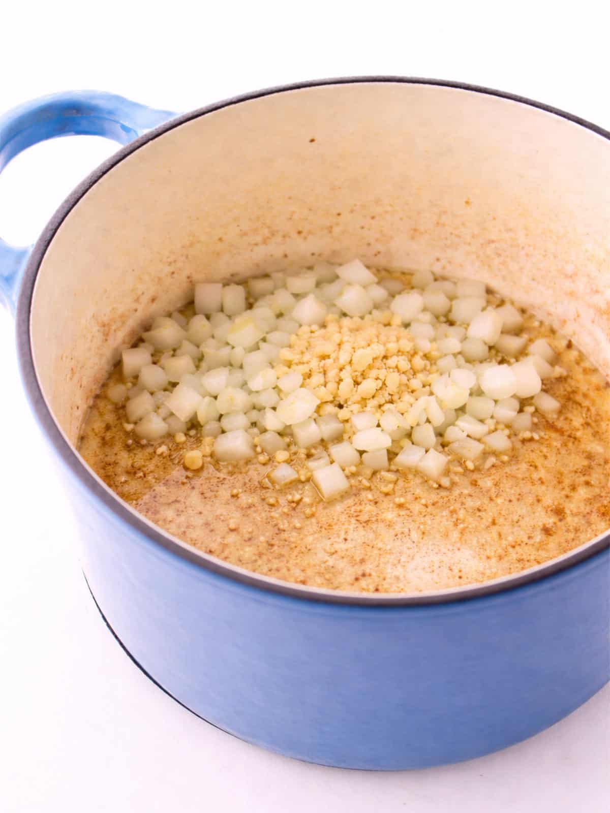 Chopped onion and garlic cooking in a blue Dutch oven.