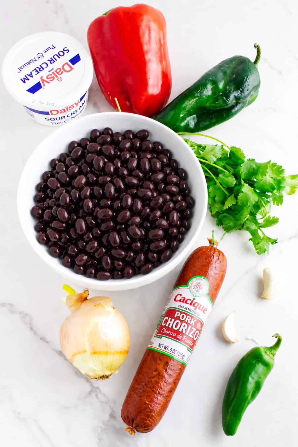 Ingredients for chorizo refried beans including black beans, Mexican chorizo, peppers, onion, garlic, and cilantro.