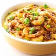 Casserole dish of blackened shrimp on grits garnished with green onion.