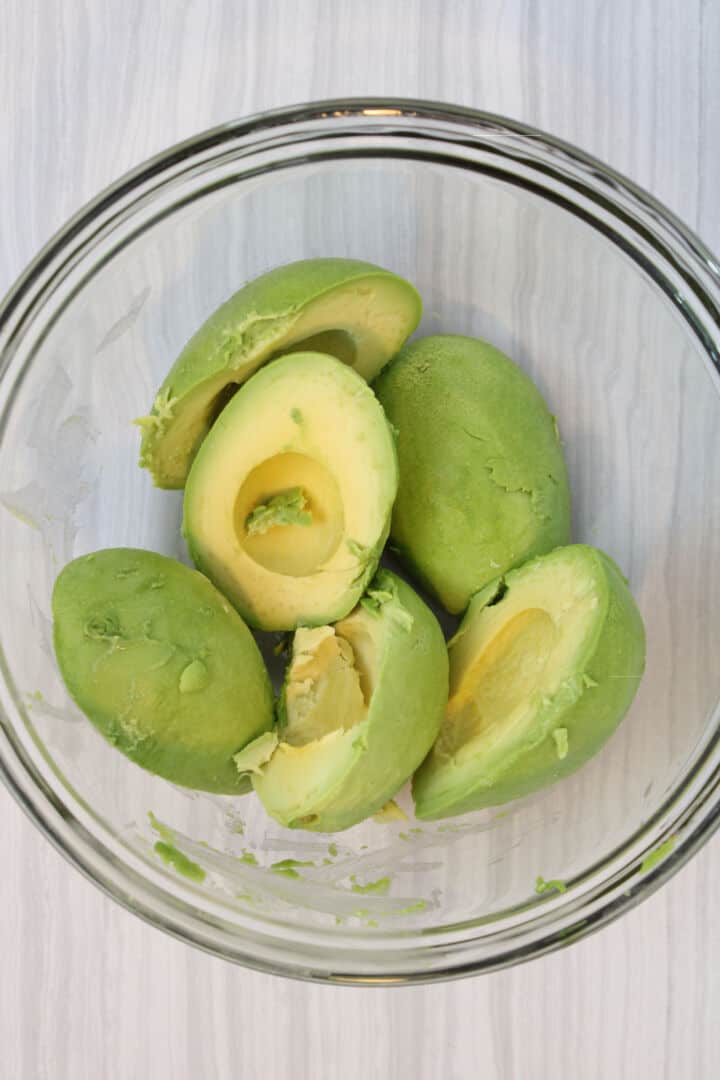 Peeled avocado halves in a mixing bowl for making guacamole.