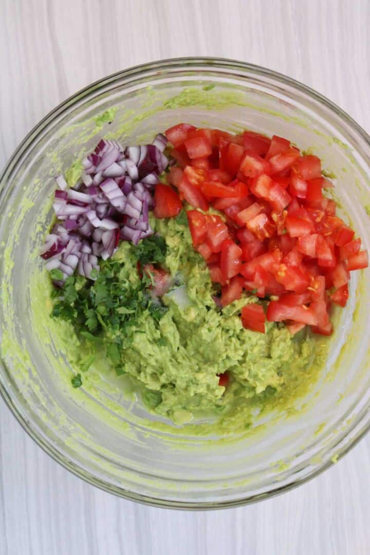 Mashed avocado with chopped onion, tomato, and cilantro for guacamole.