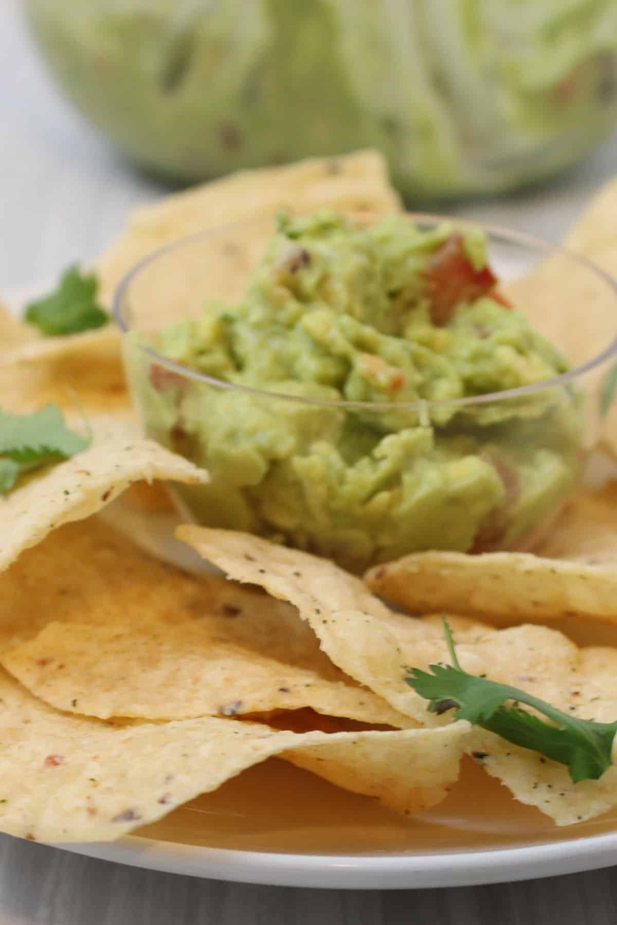 Bowl of guacamole with a large bowl of chips in the background.