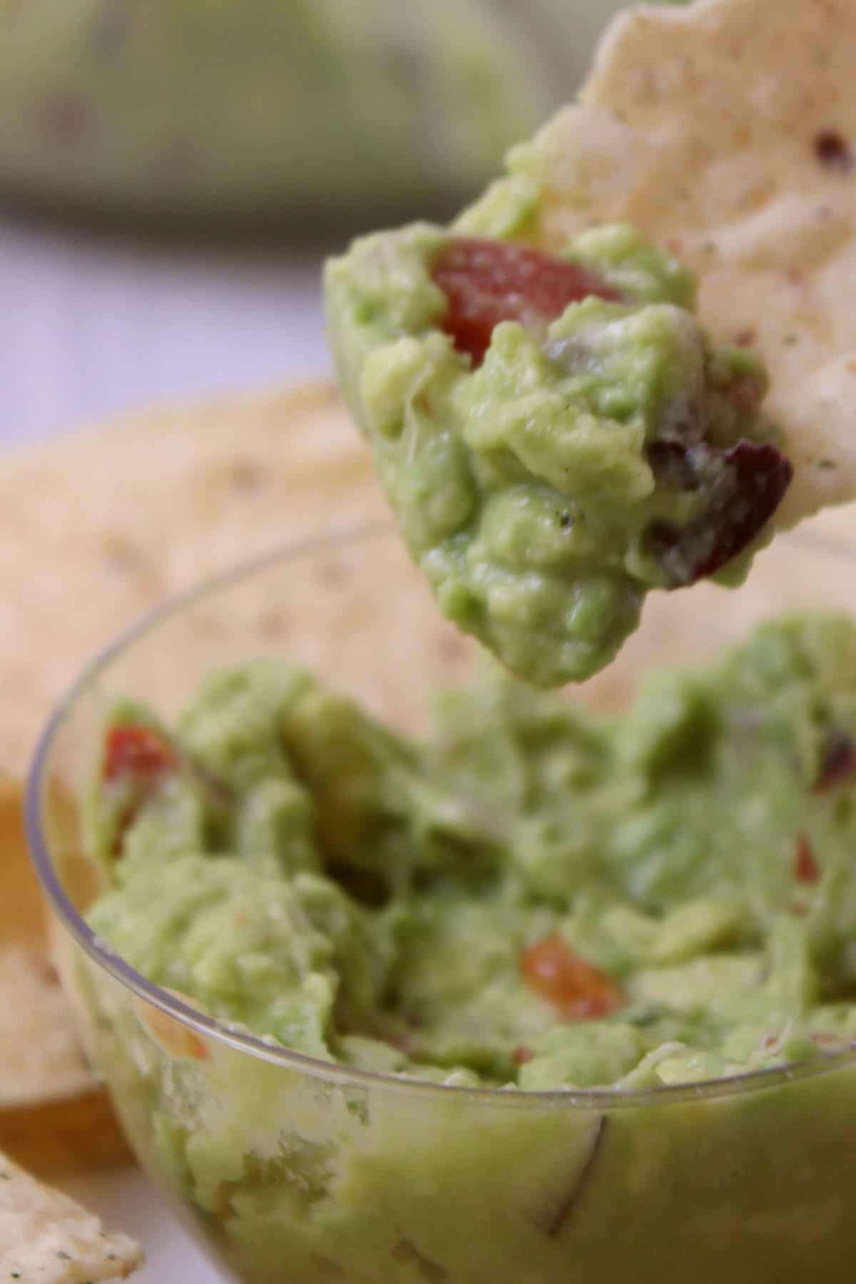 A tortilla chip being dipped into a bowl of guacamole.