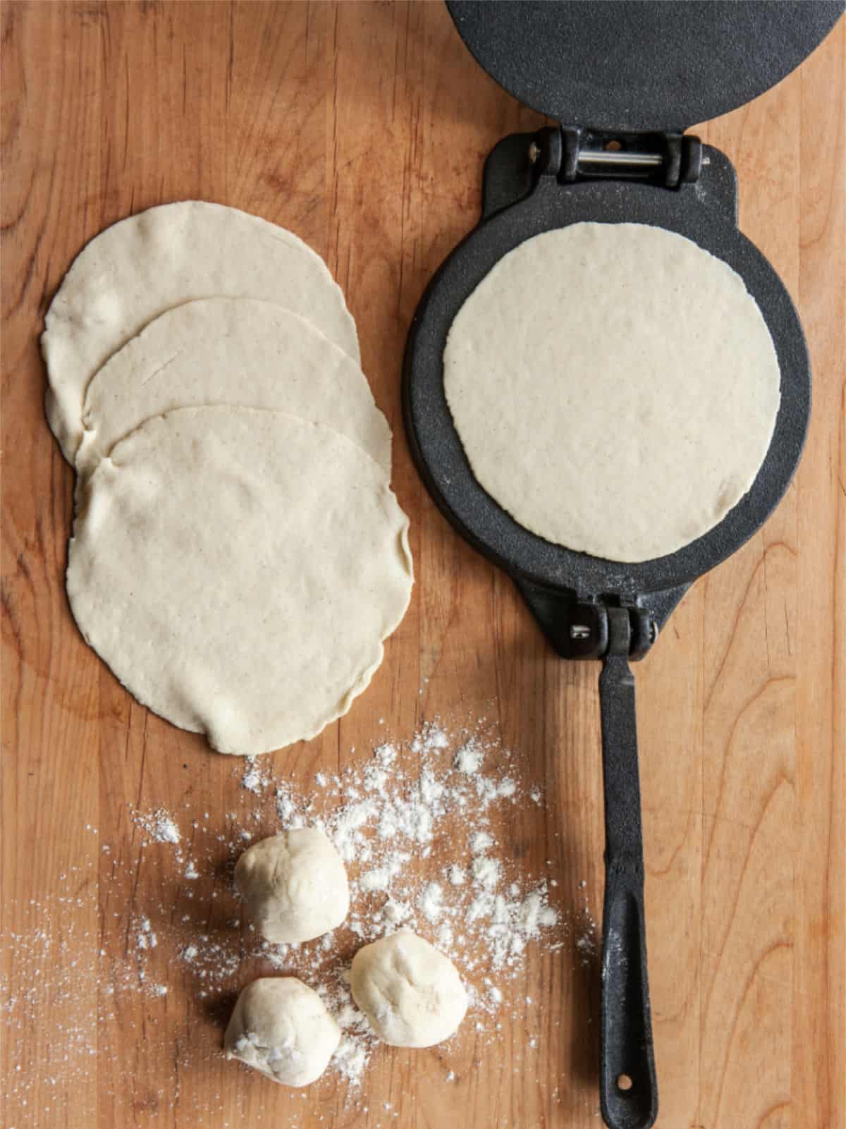 Flour tortilla dough pressed into a thin rounds on a lightly floured surface.