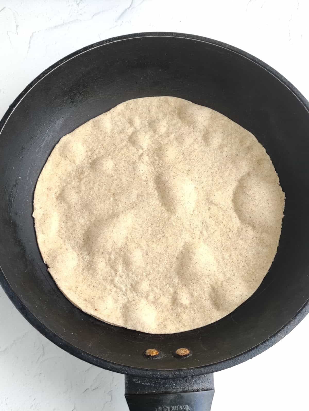 Flour tortilla cooking in a hot skillet with bubbles forming.