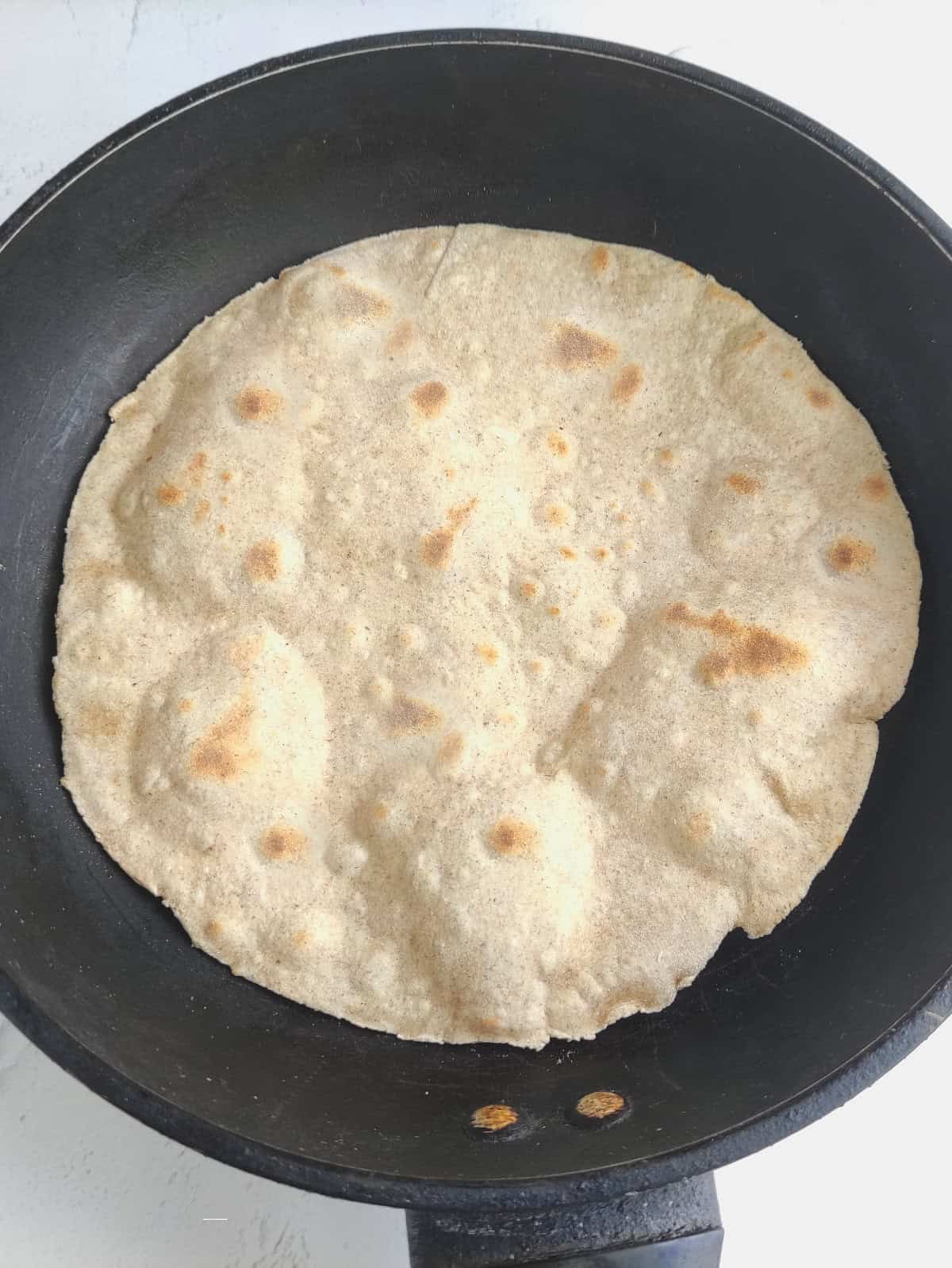 Homemade flour tortilla cooking in a skillet with golden brown spots.