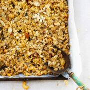 baked granola on a sheet pan with a blue handled scoop.