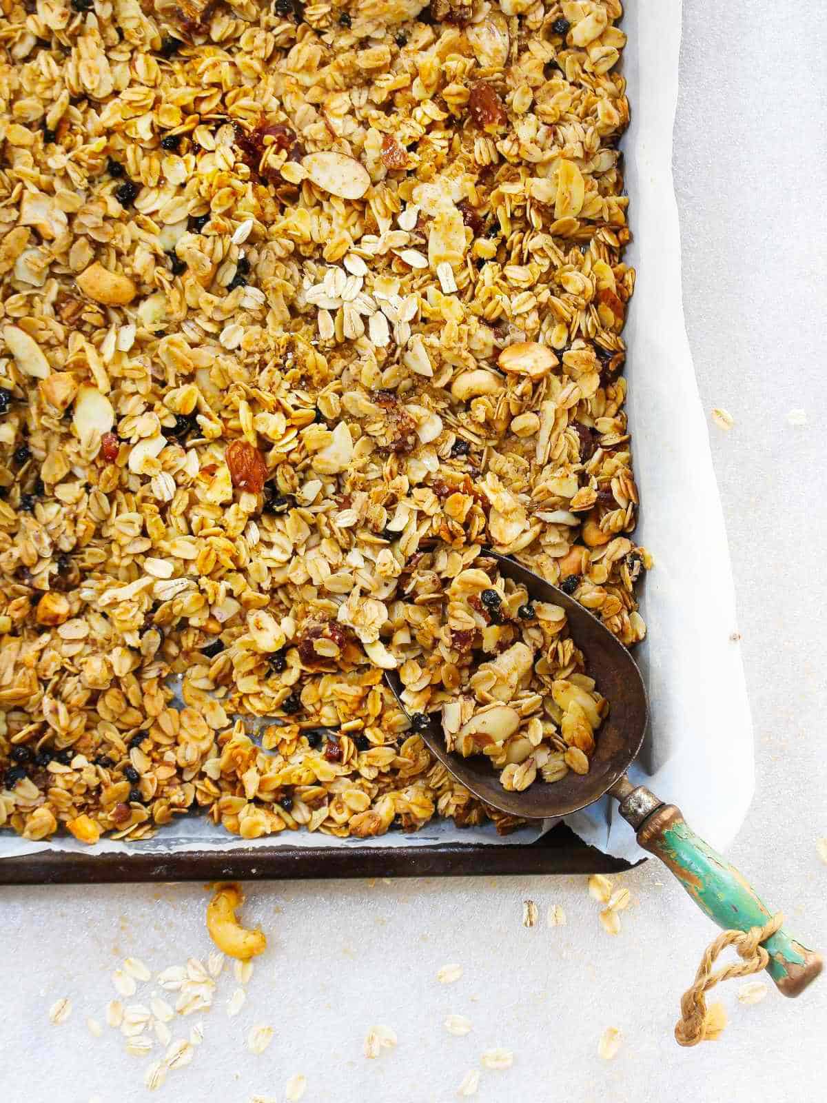 baked almond vanilla granola on a sheet pan with a blue handled scoop.