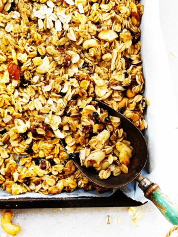 baked granola on a sheet pan with a blue handled scoop.