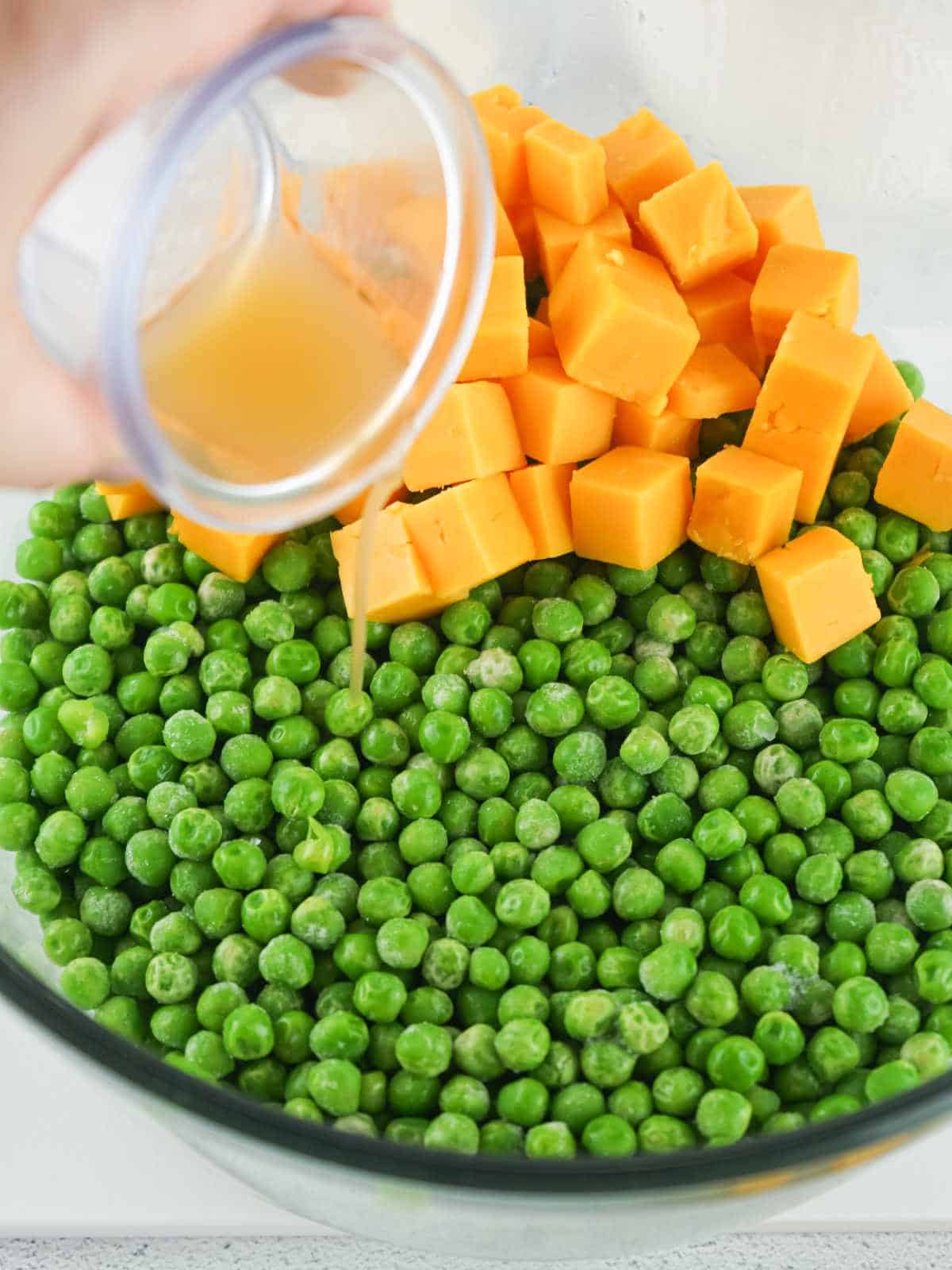 cheese and dressing on top of green peas in a bowl.