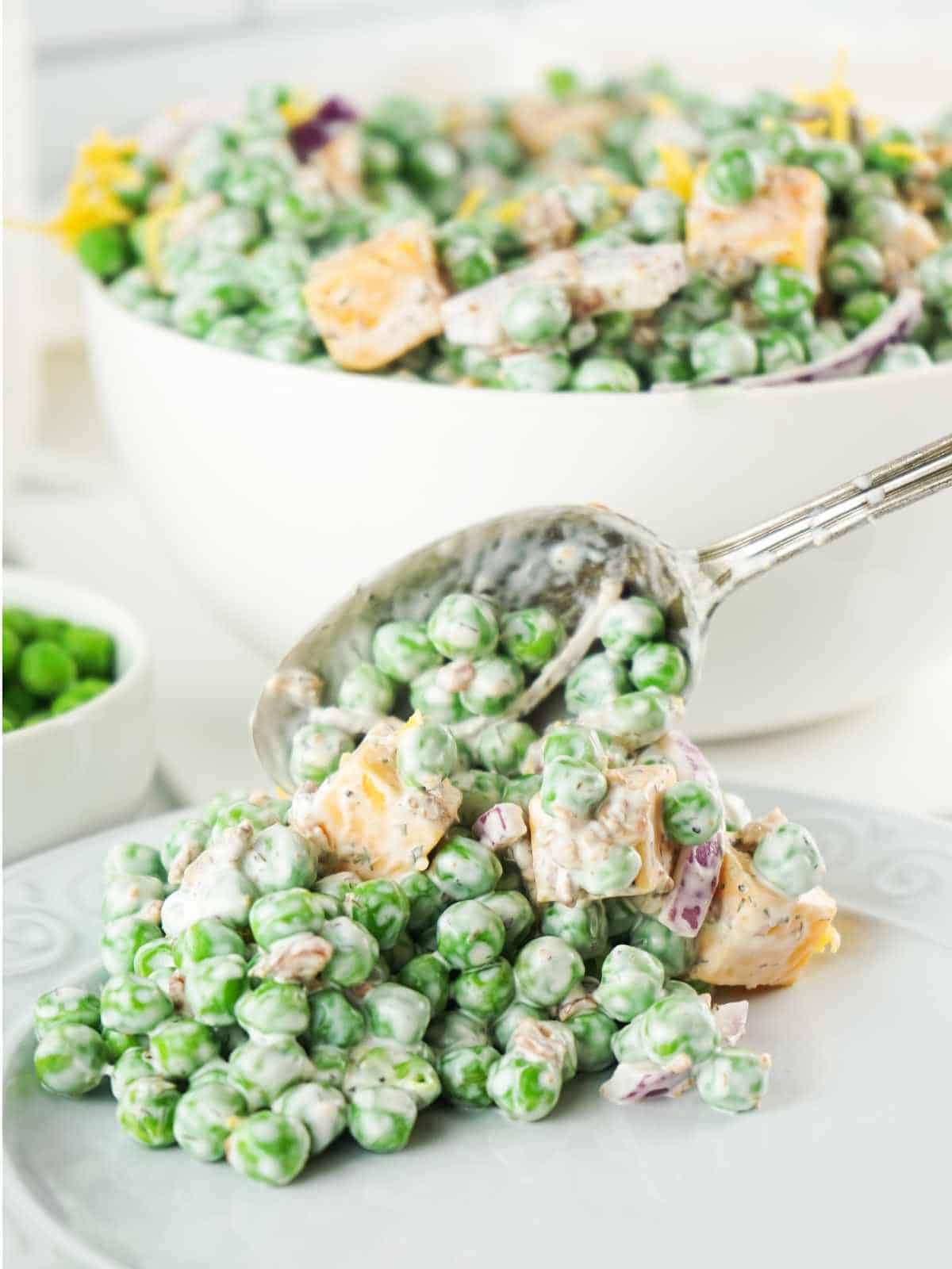 spoonful of English pea salad on a plate with bowl in background.