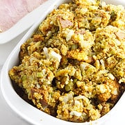 cornbread stuffing in a casserole dish with a sliced ham in the background.