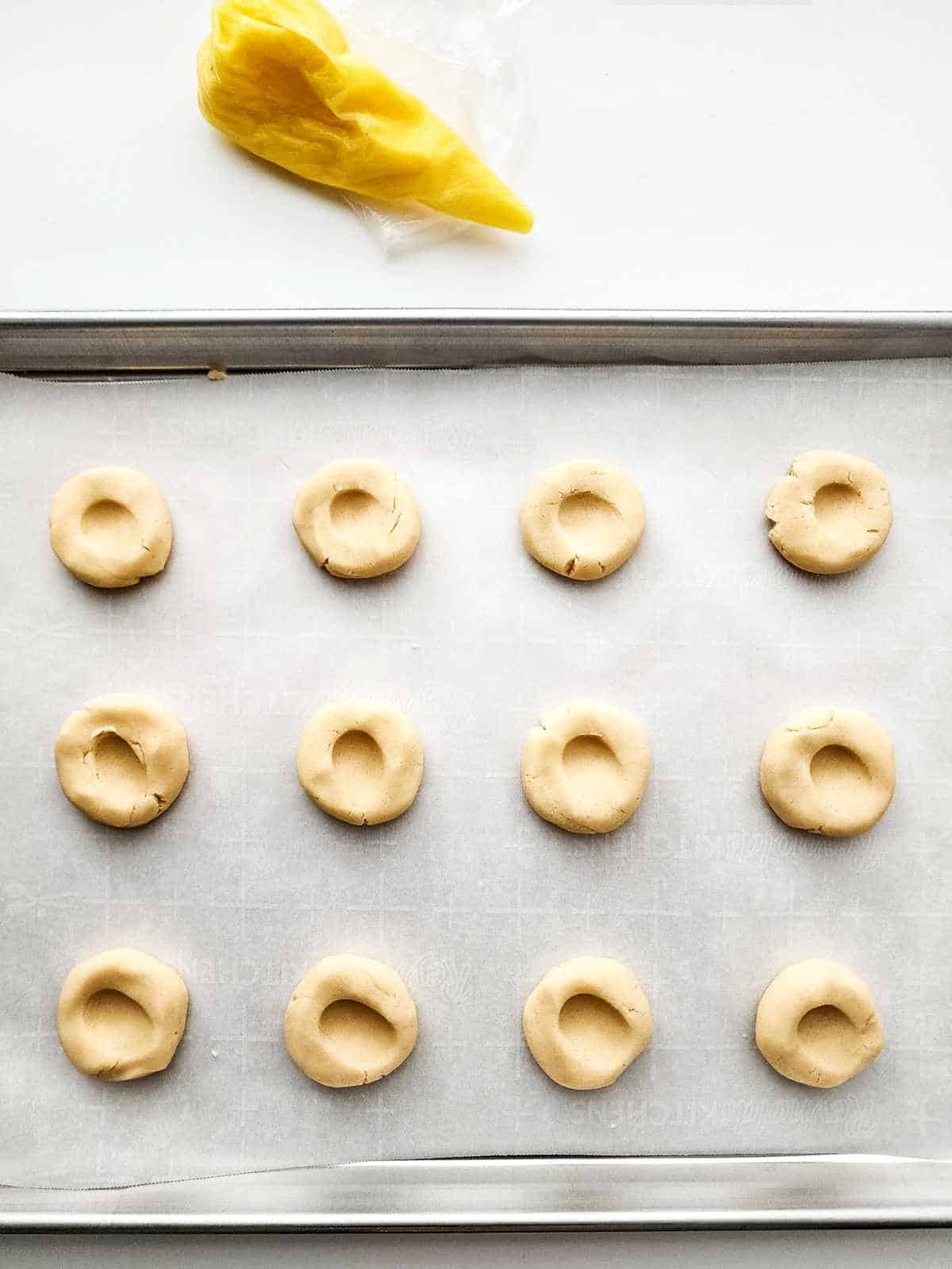 cookies on a parchment lined cookie sheet with indentations in the center of each cookie.
