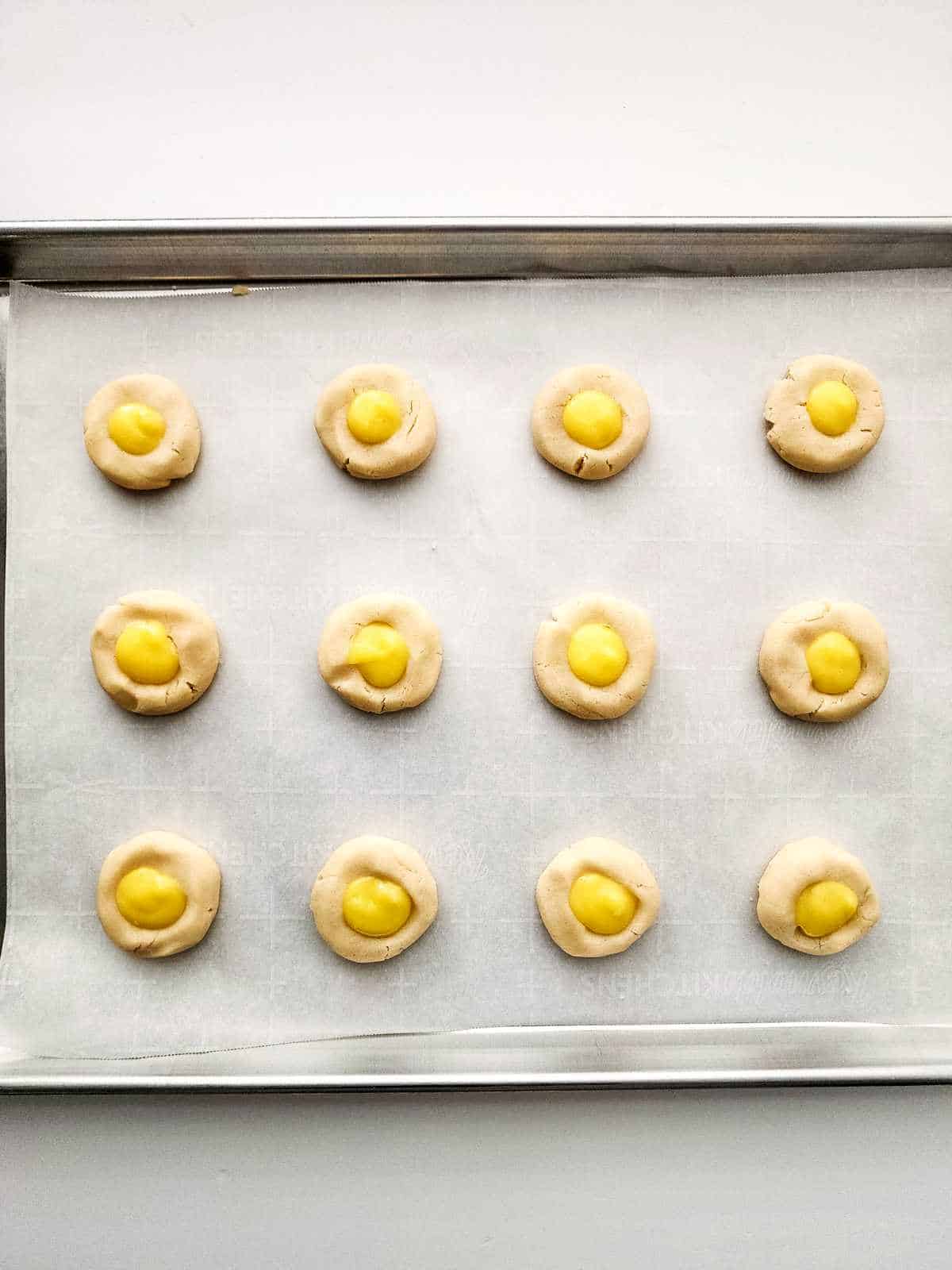 piped lemon curd in the indentation of each cookie on a cookie sheet.