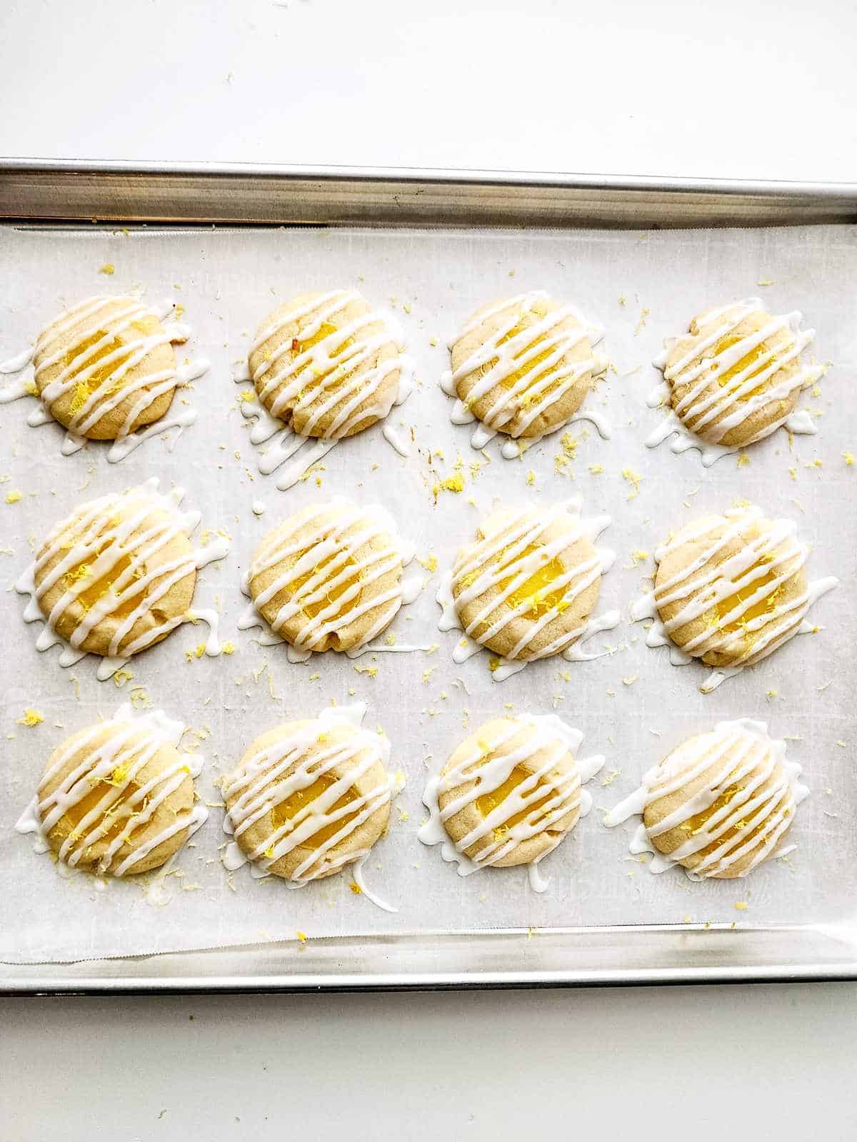 icing drizzled in a zig zag pattern on each lemon curd filled cookie sitting on a cookie sheet.