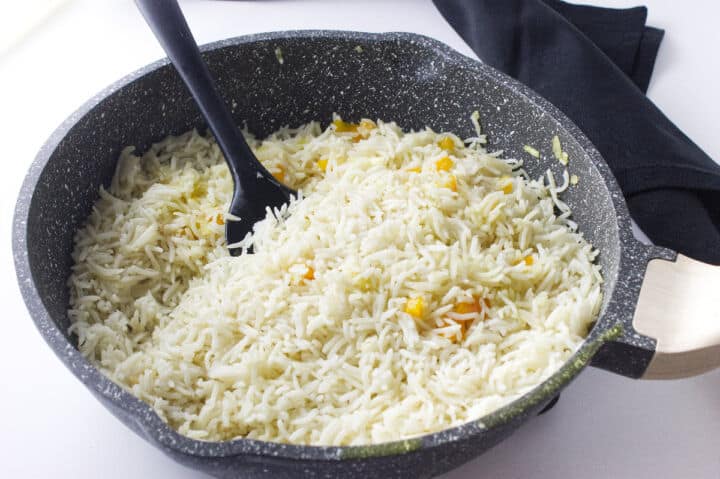 Rice in a skillet with onion and red bell pepper.