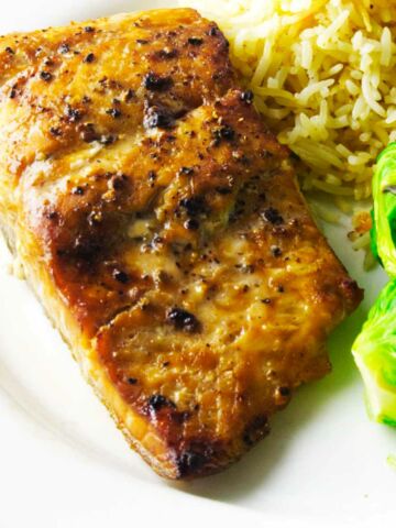 Salmon filet in a serving dish with rice pilaf and brussels sprouts.