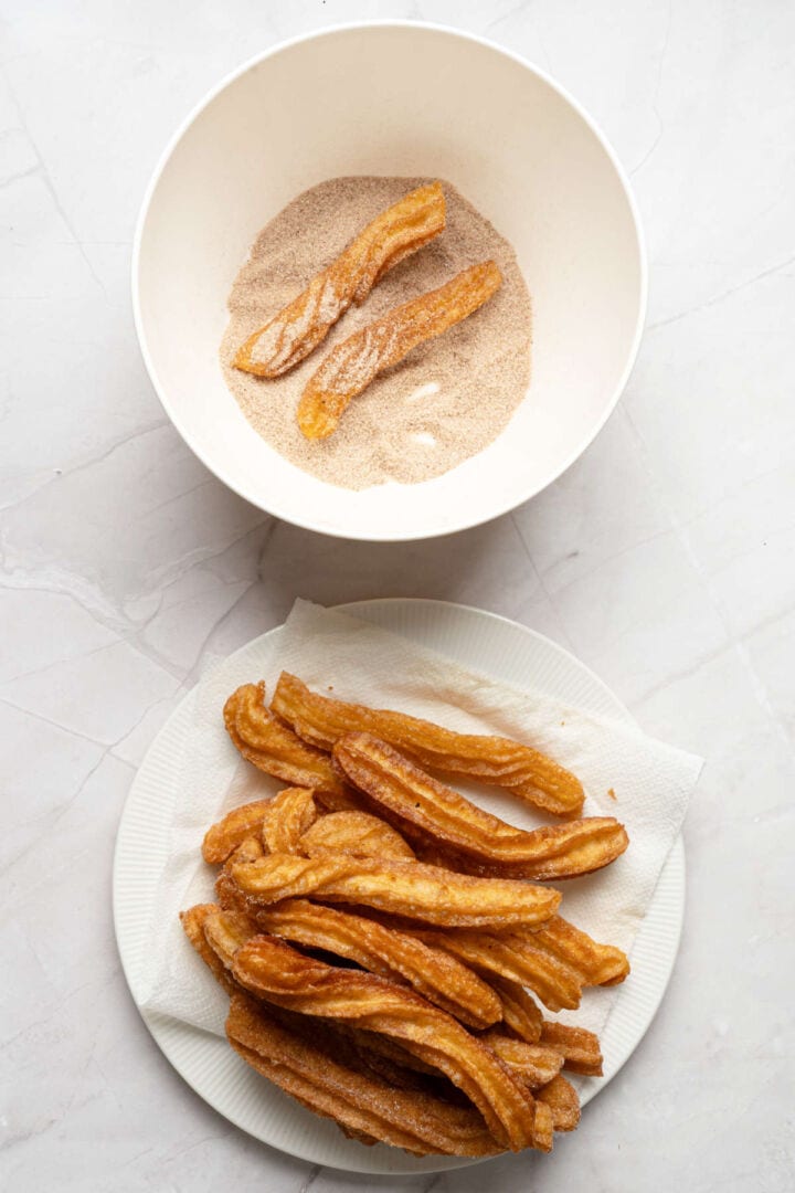 Coating freshly fried churros in cinnamon sugar.