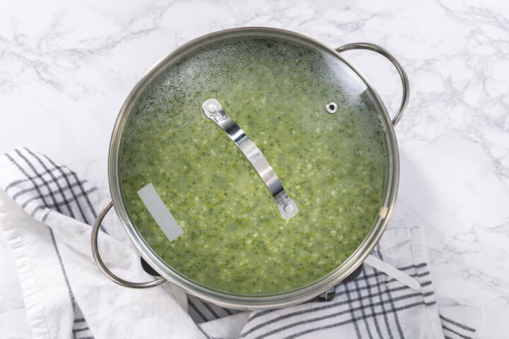 Arroz verde simmering covered in a pot with a glass lid as the rice absorbs the liquid.