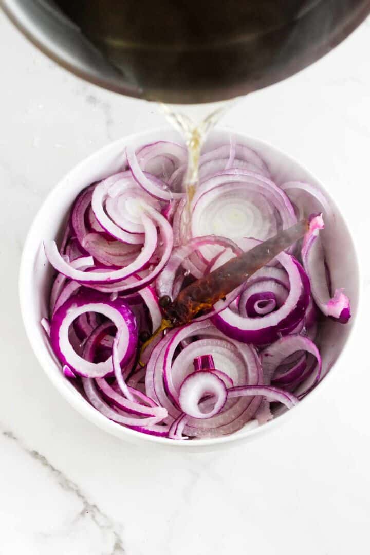 Pouring hot pickling brine over bowl of sliced red onions.