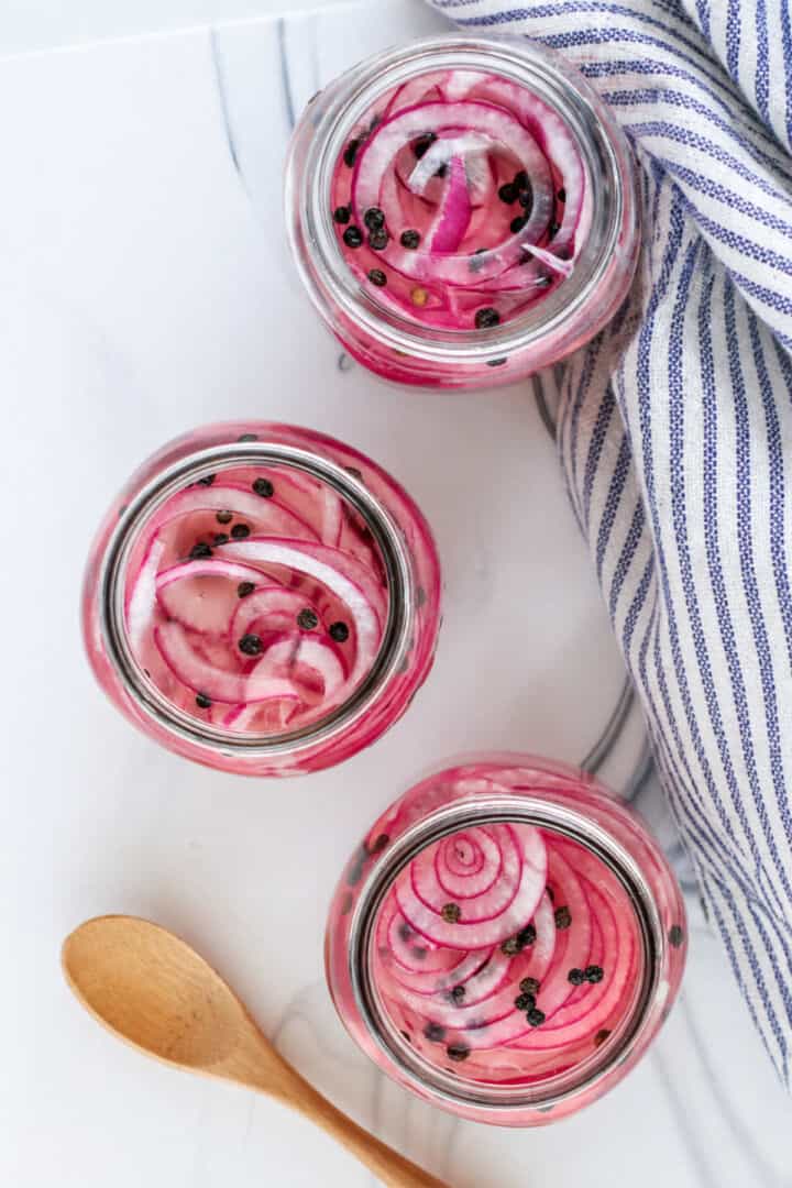 Jars filled with Mexican pickled red onions on a striped towel.