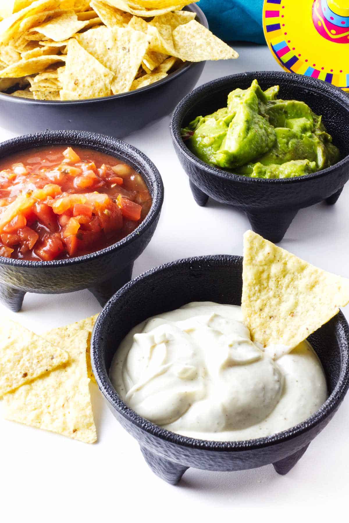 Mexican white sauce, pico de gallo, guacamole, and chips in separate bowls.