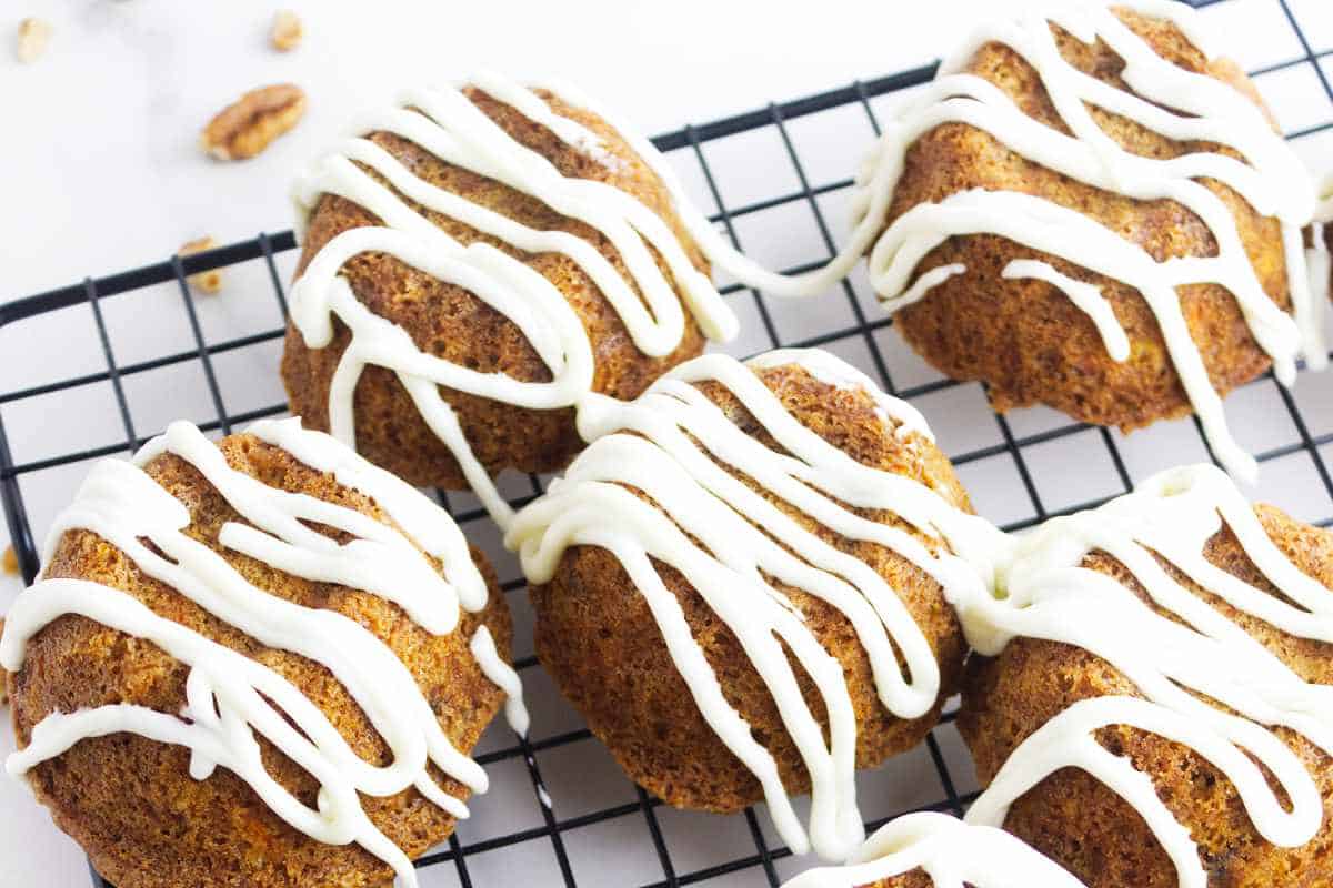 mini carrots cakes drizzled with cream cheese frosting on a cooling rack.