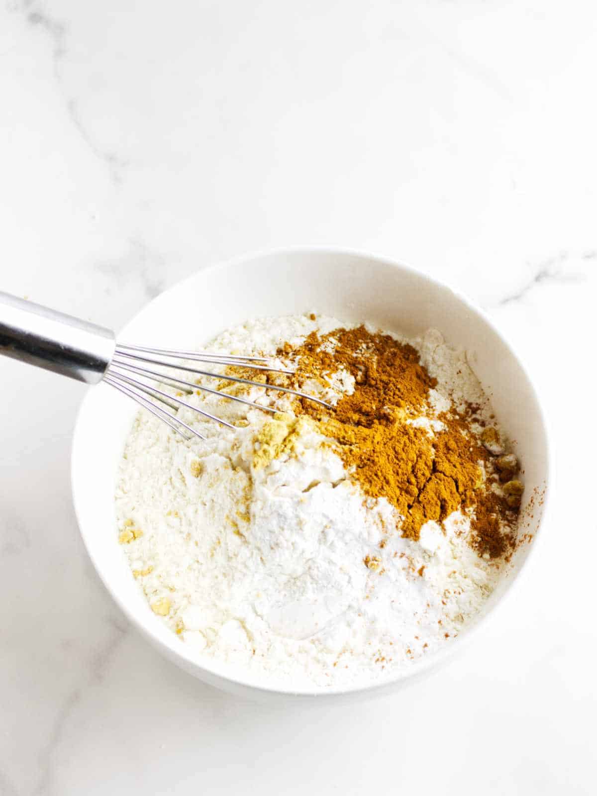 flour, spices, salt, and baking powder in a bowl with a whisk.