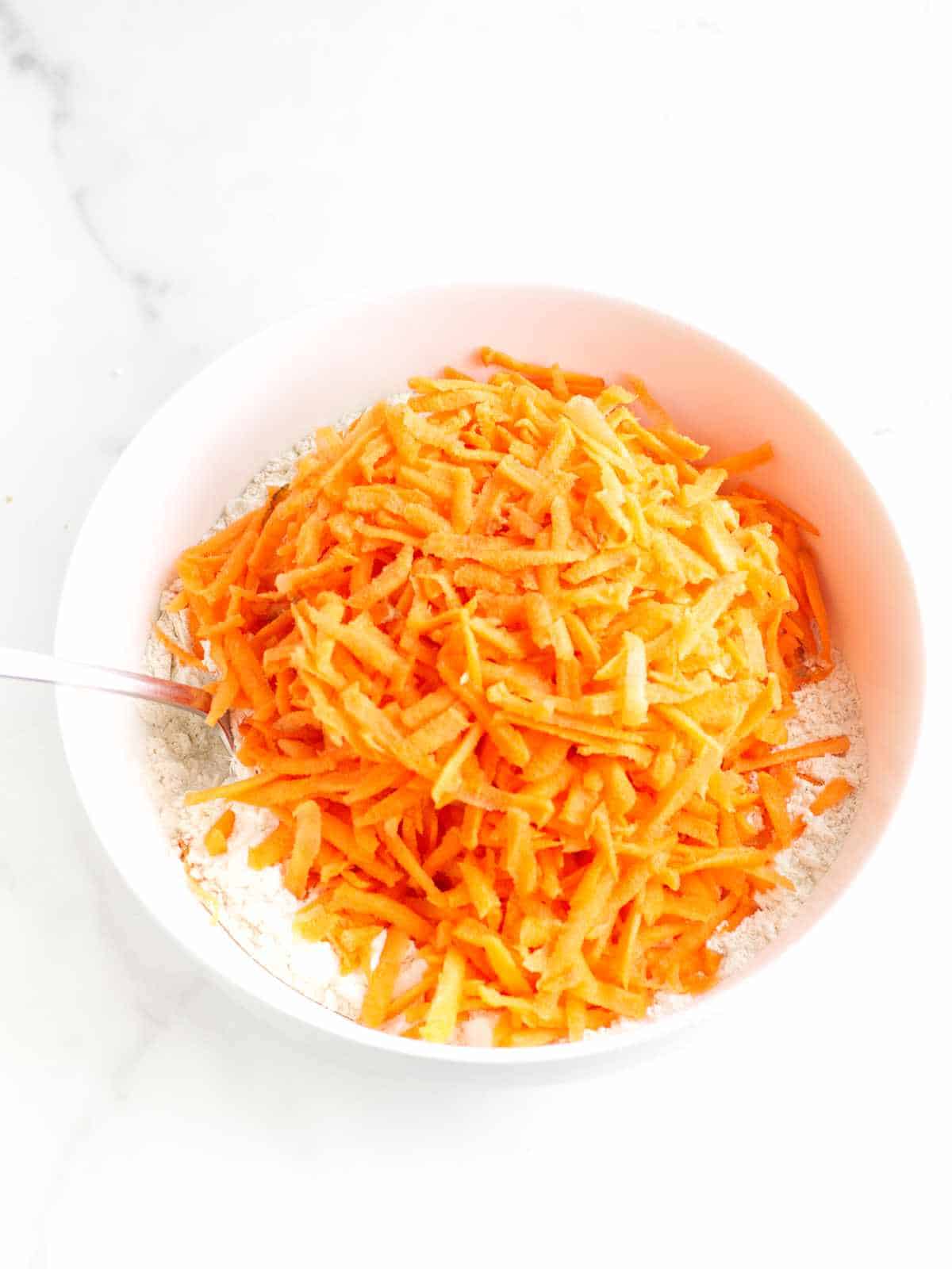 grated carrots in a bowl on top of flour.