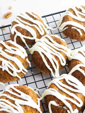 mini carrots cakes drizzled with cream cheese frosting on a cooling rack.