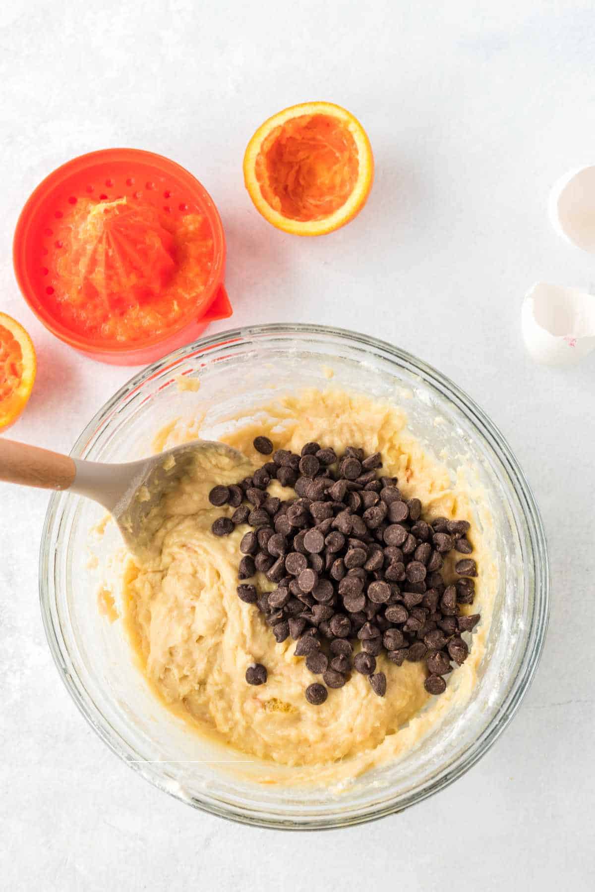 chocolate chips added to batter with orange juicer and orange nearby.