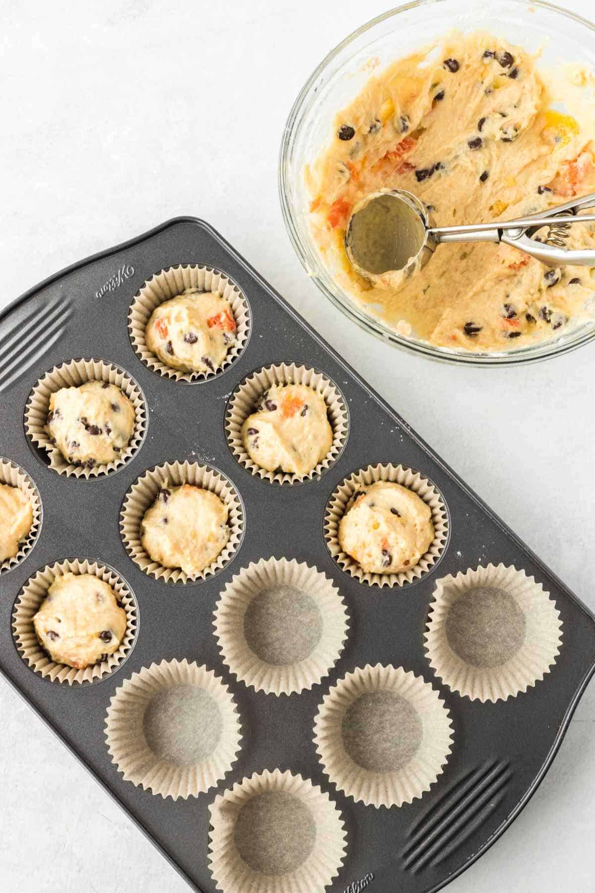 scooping batter into paper muffin tin liners on a white background.