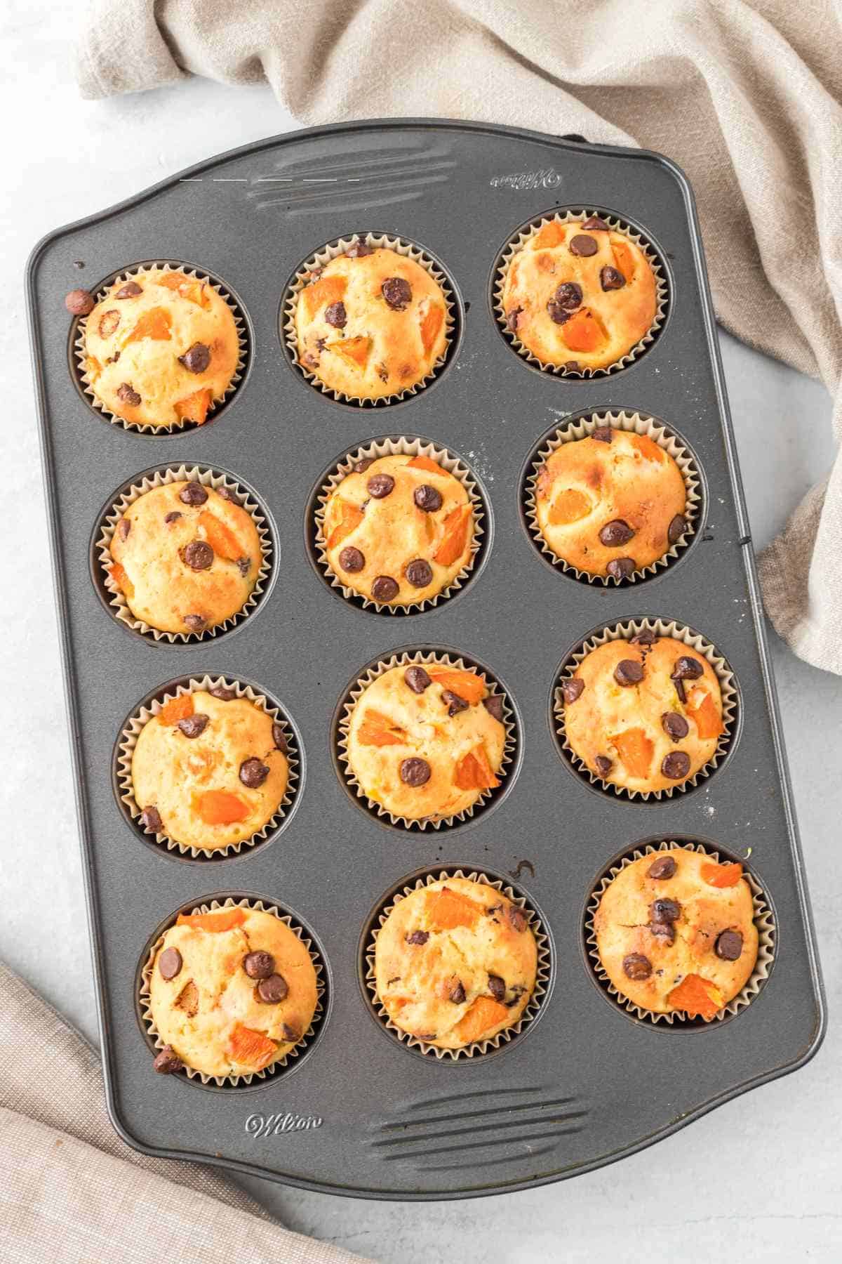 muffin tin with baked orange breakfast muffins on a white background.