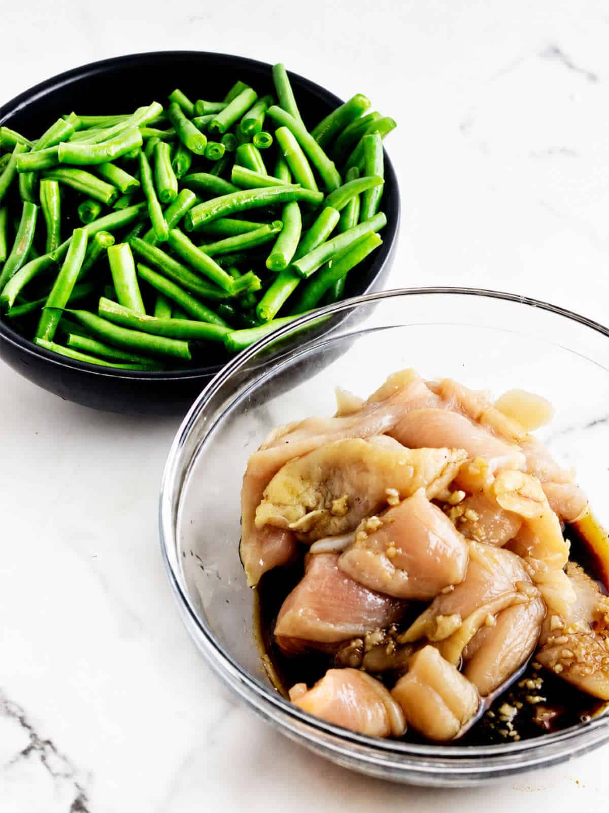 Sliced raw chicken marinating in ginger soy sauce beside a bowl of cut green beans for Panda Express String Bean Chicken.