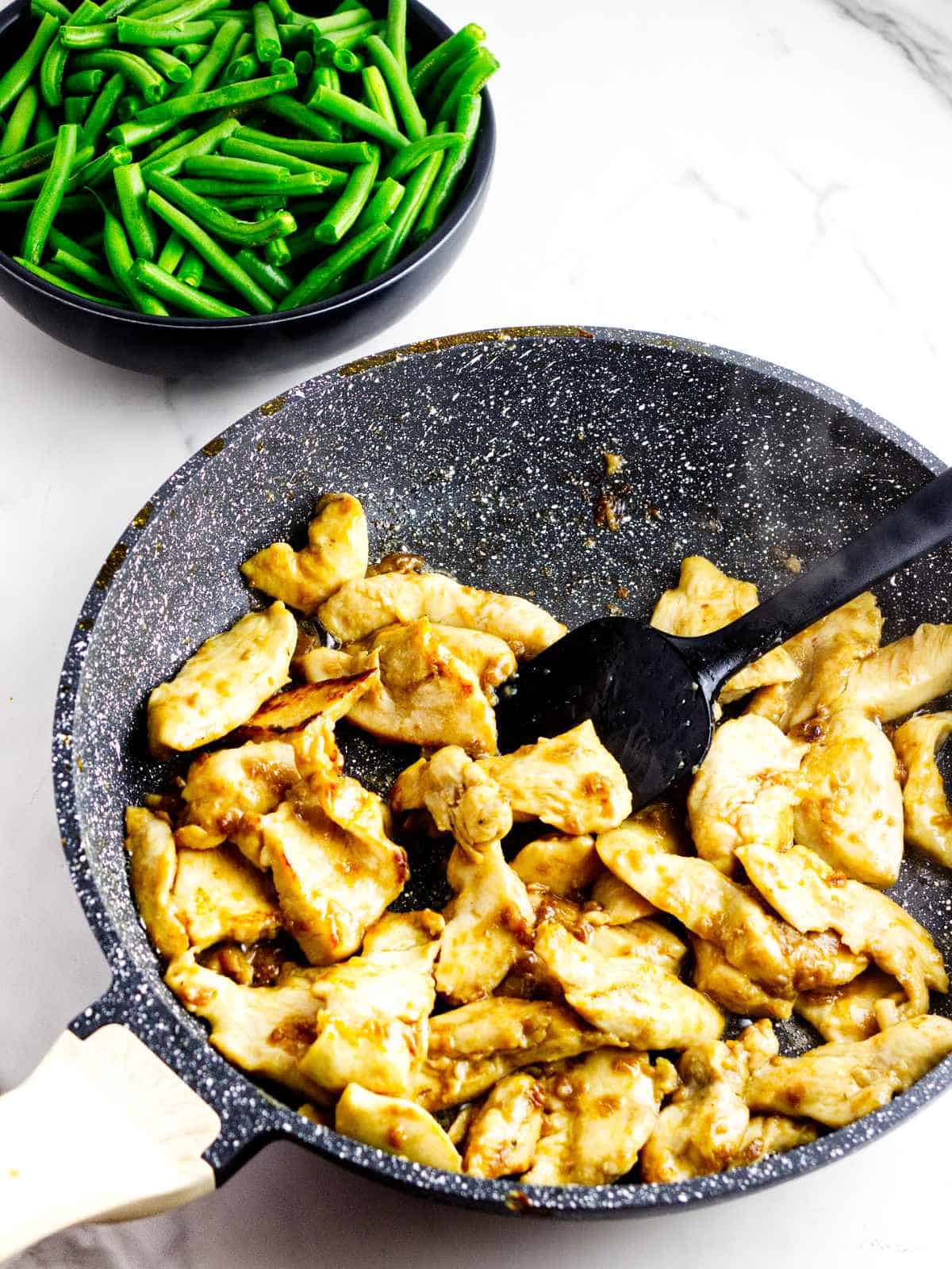 Marinated chicken slices cooking in a skillet for Panda Express String Bean Chicken copycat.