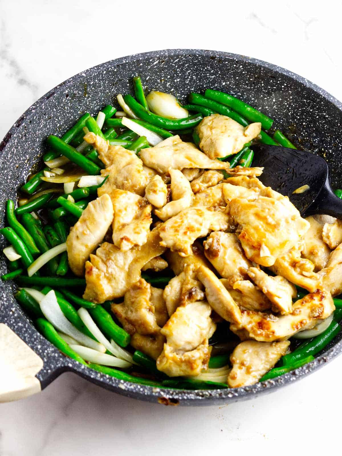 Chicken, green beans, and onions tossed together in a skillet for Panda Express String Bean Chicken.