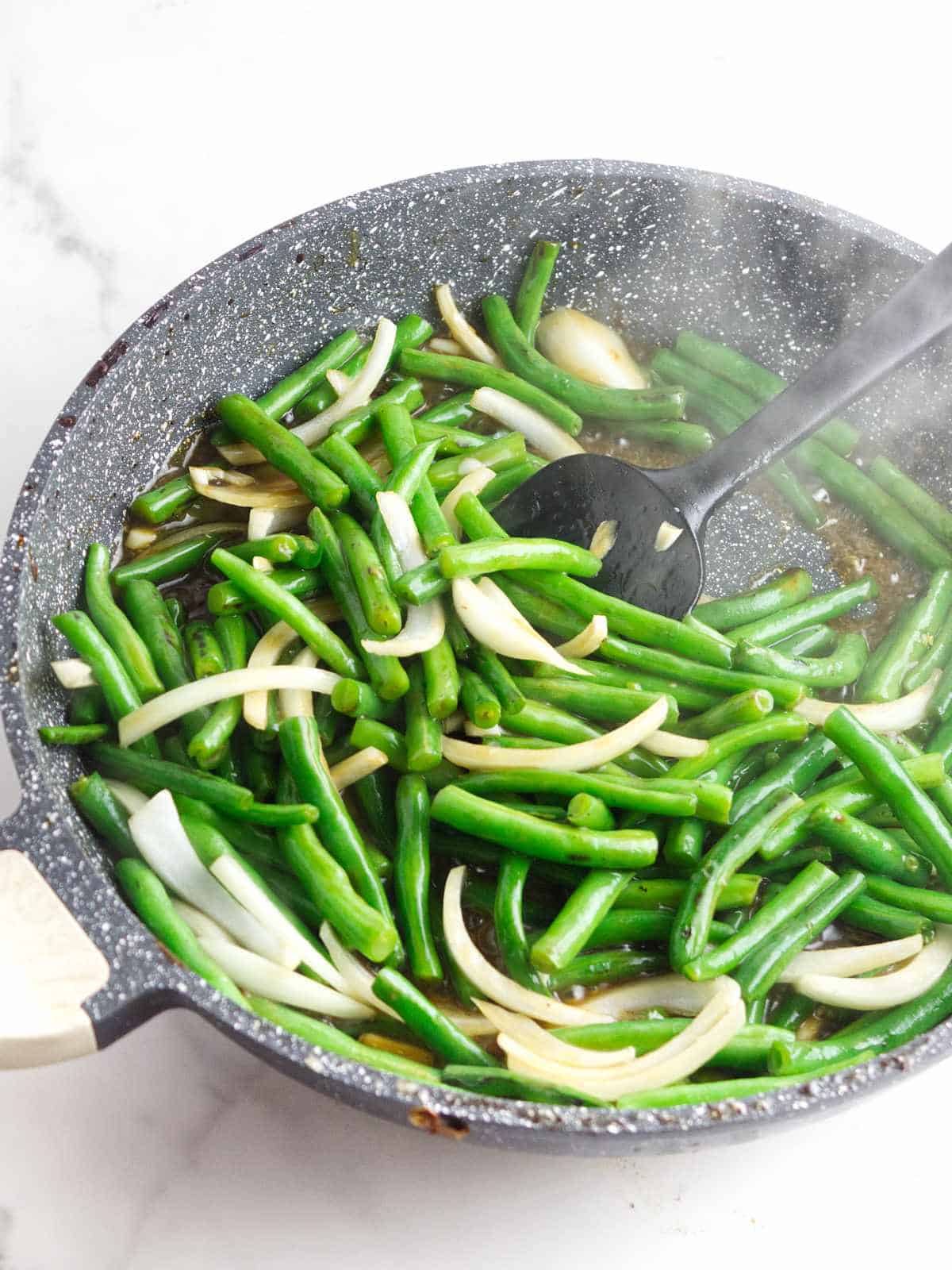 green beans and slivered onion in a skillet getting sauteed.