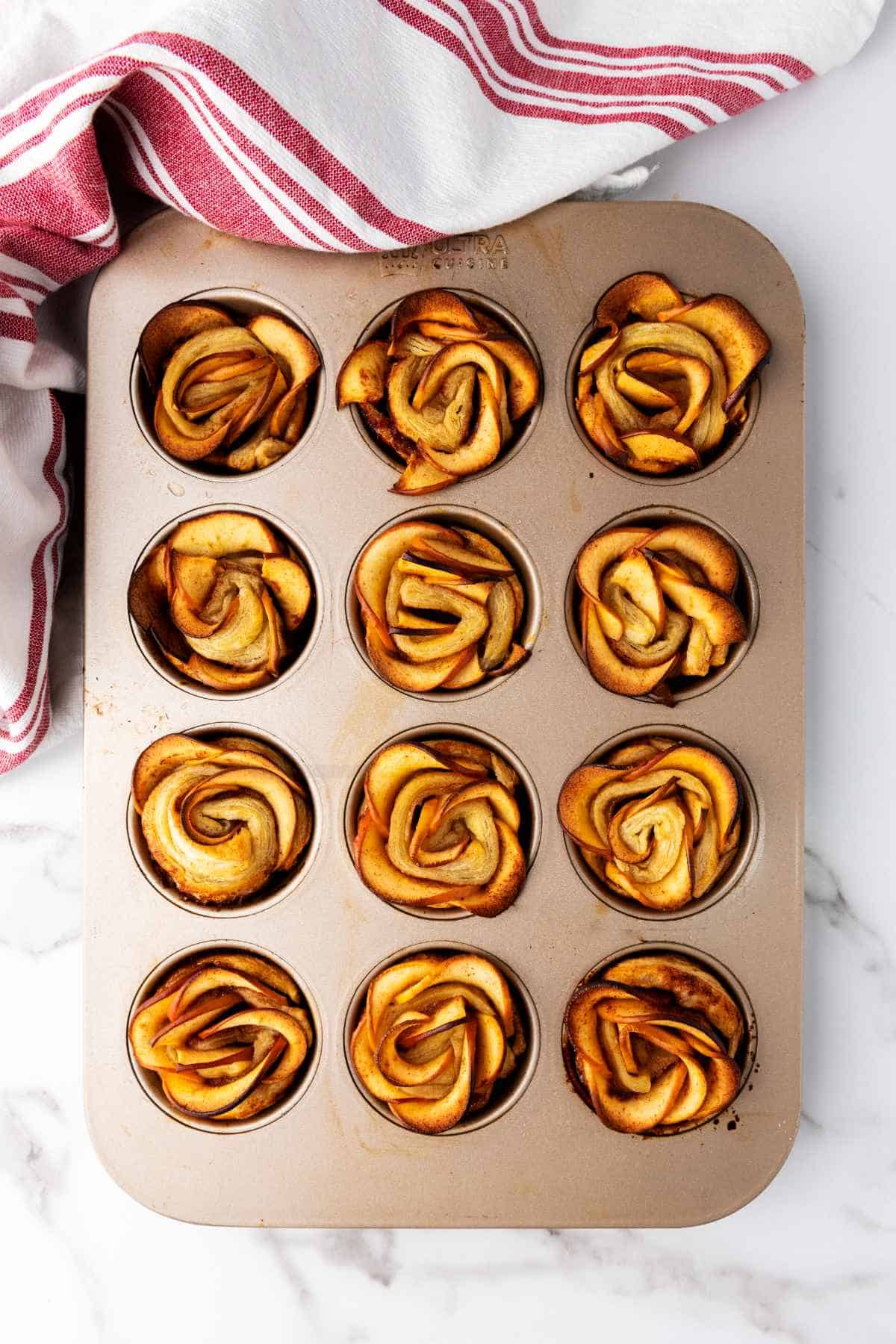 baked puff pastry apple roses in a muffin pan.