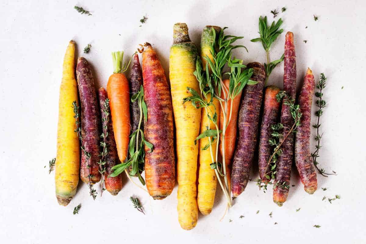 raw rainbow carrots on a counter top with sprigs of herbs.