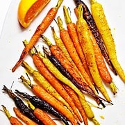 serving platter of tri color carrots garnished with herbs, olive oil, and lemon.