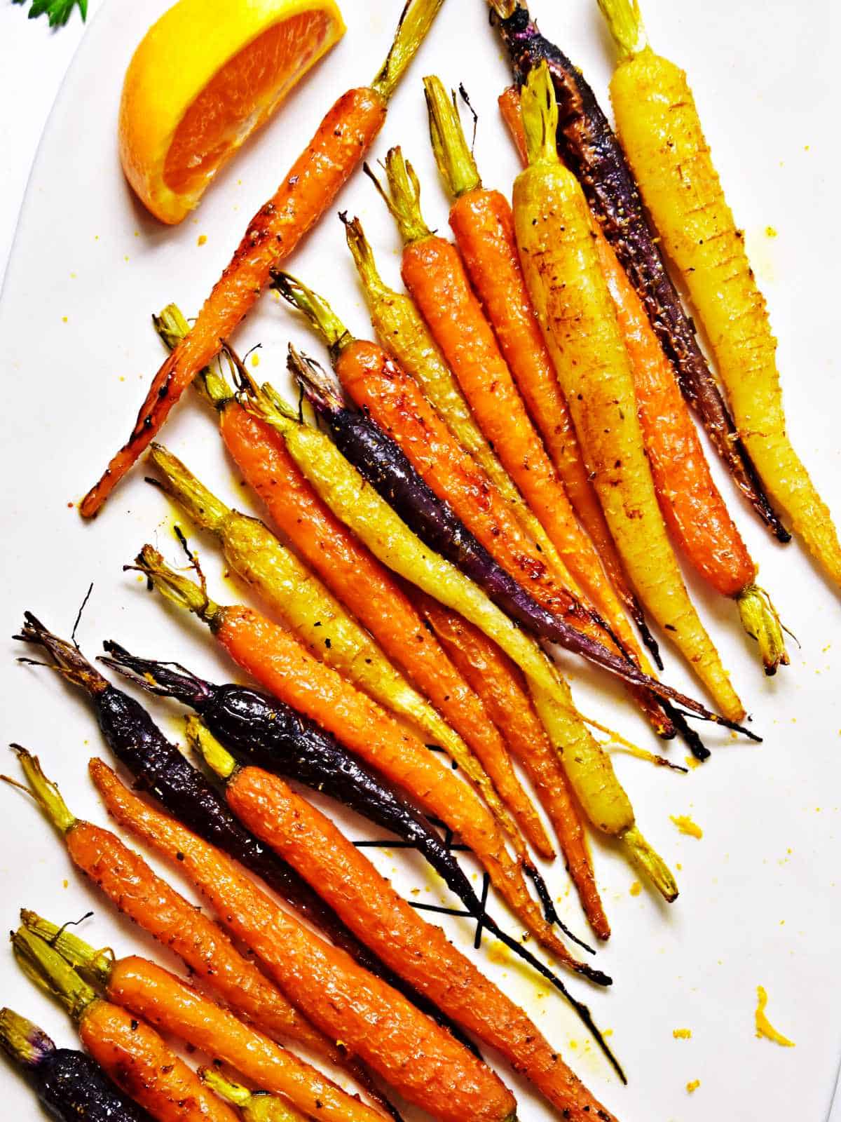 serving platter of tri color carrots garnished with herbs, olive oil, and lemon.