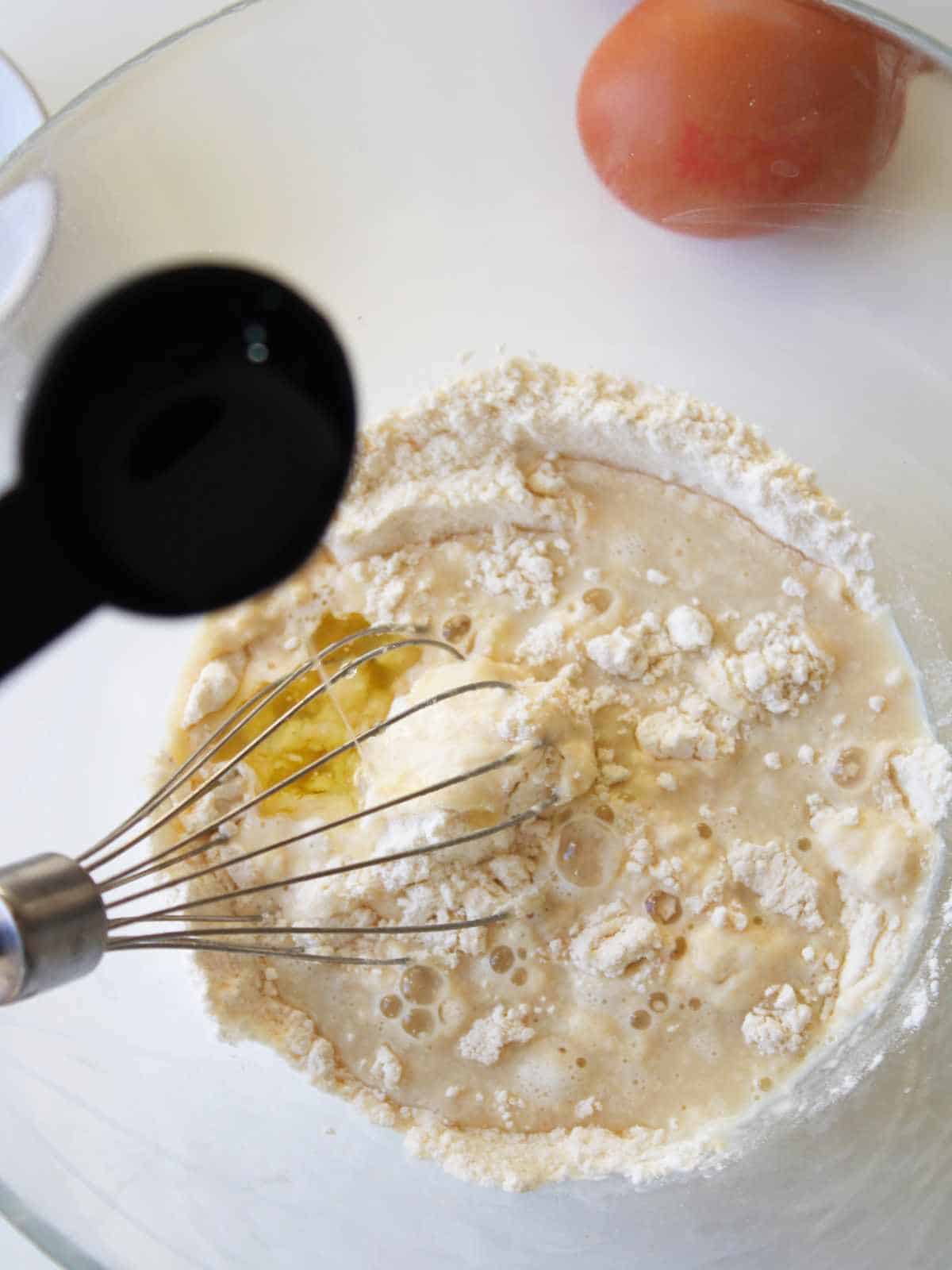 whisk in a bowl of flour mixture with egg nearby.
