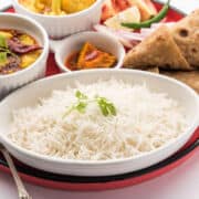 A brass spoon holds a small serving of cooked white basmati rice against a plain white background.