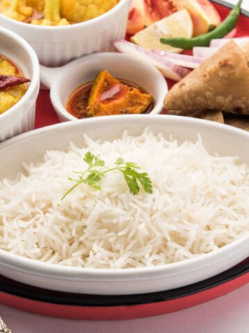 A brass spoon holds a small serving of cooked white basmati rice against a plain white background.