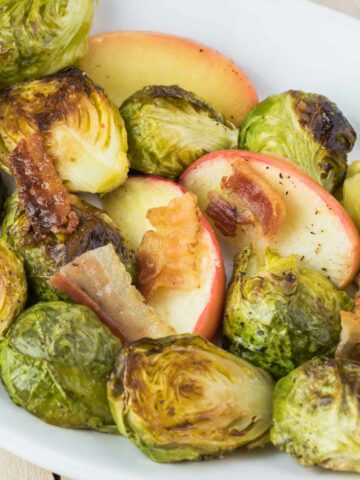 Serving bowl with roasted brussels sprouts and sliced granny smith apples.